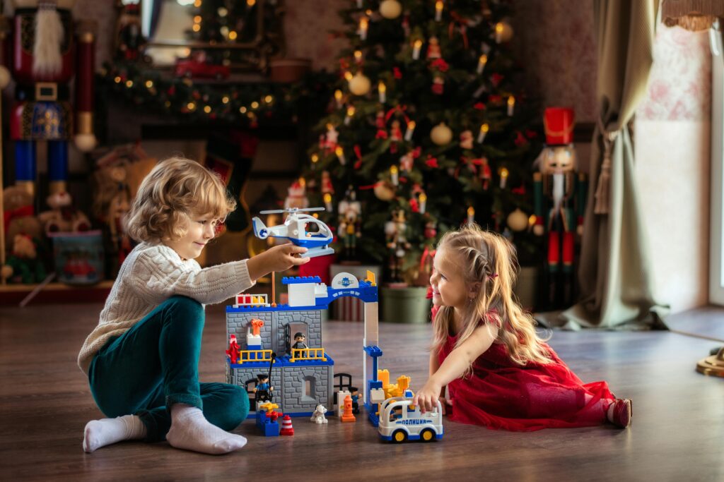 Two children enjoy playing with toys near a decorated Christmas tree, capturing festive joy.